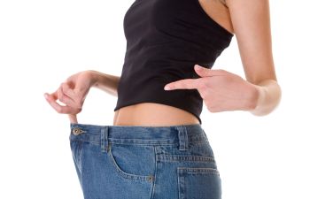 A slim woman after weight loss treatment posing in her old huge pair of jeans.