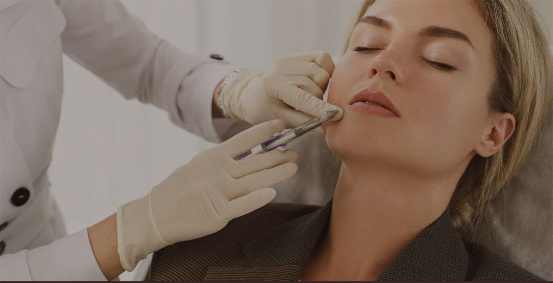 A person receives a cosmetic injection in the chin area by a professional wearing gloves.