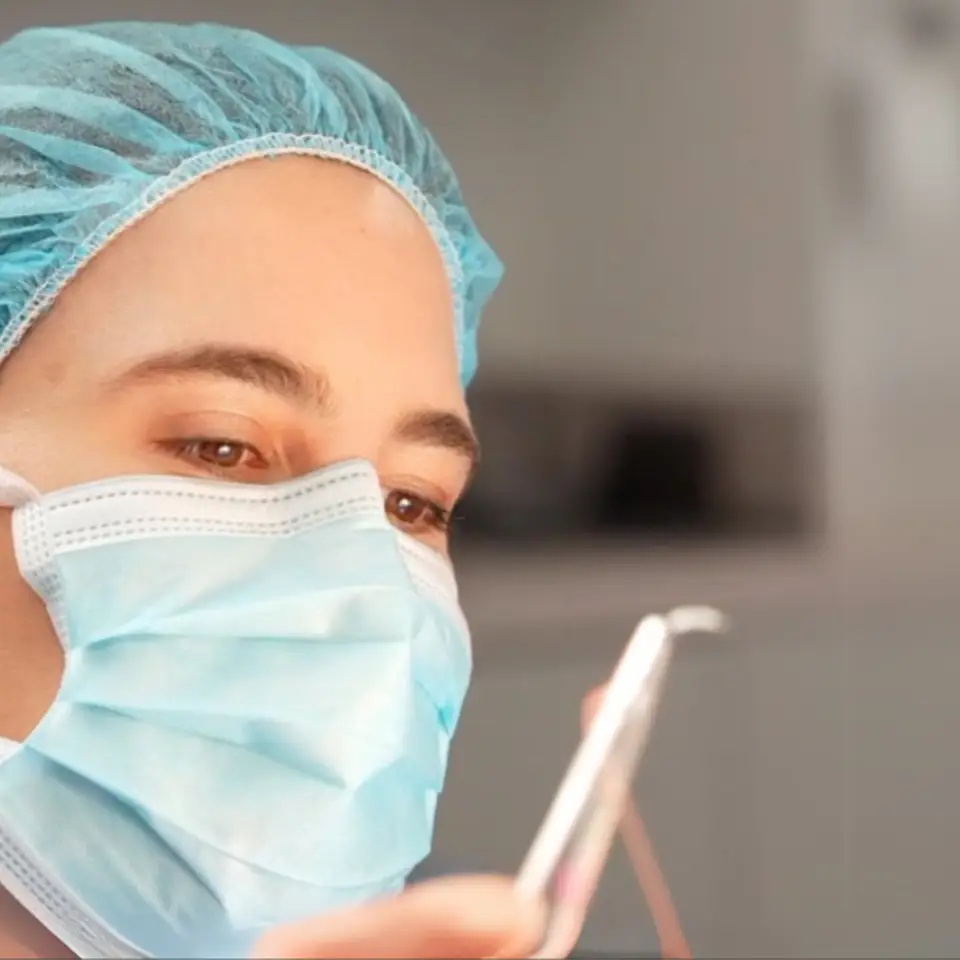 A person wearing a blue surgical cap and face mask looks intently at a dental tool in a clinical setting.
