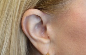 Close-up of a person's ear with straight blonde hair, wearing a gold hoop earring.